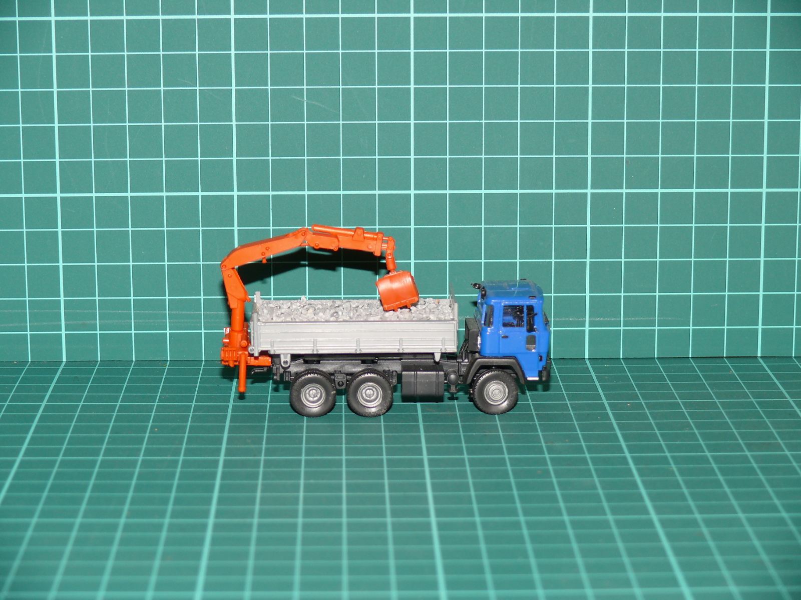 Herpa - Roman Diesel / MAN Třínápravový sklápěč se zadním drapákem a nákladem štěrku – H0