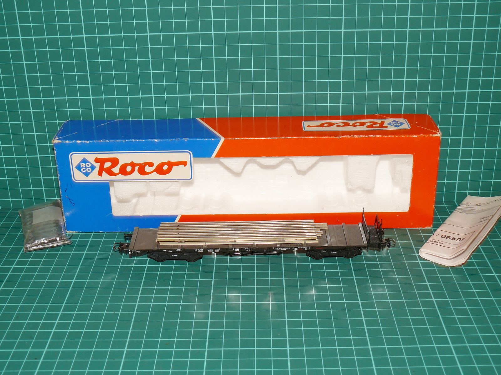 ROCO H0 – Čtyřnápravový plošinový klanicový vůz řady Rlmmp-700 DB s nákladem ocelových trubek (kat. č. 46490 / DC) v krabičce s doplňky – H0